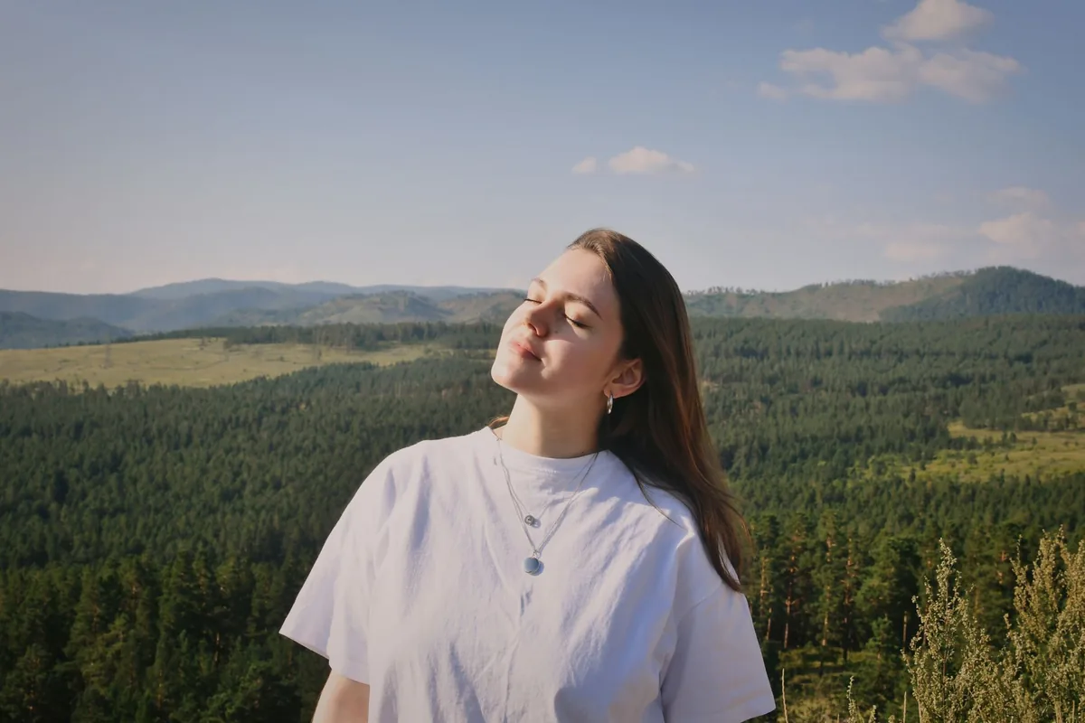 Žena se zavřenýma očima se nadechuje v krajině